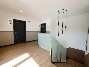 Distribuidor de planta en la Pensión Casa Cancela con acceso a habitaciones, barandilla de cristal, suelo de madera y lámparas modernas de diseño.