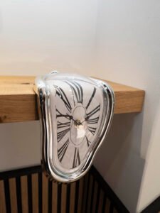 Reloj de mesa derretido de estilo surrealista inspirado en Salvador Dalí colocado sobre una estantería de madera clara.