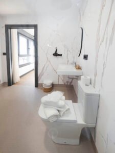 Interior de baño privado en Casa Cancela, Palas de Rei, equipado con set de toallas blancas, secador de pelo, artículos de aseo de cortesía y un diseño moderno con revestimiento de mármol.