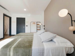 Vista lateral de habitación doble en Casa Cancela, Palas de Rei, mostrando el acceso al baño privado, aire acondicionado y una decoración moderna y minimalista.