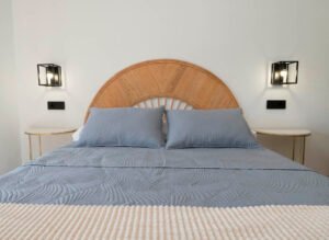 Plano detalle de la cama matrimonial con un original cabecero semicircular de mimbre artesanal y lámparas de diseño rústico-industrial en Casa Cancela, Palas de Rei.