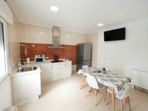 Zona de cocina y comedor en el apartamento integrado de Casa Cancela, Palas de Rei. Un espacio moderno y funcional equipado con electrodomésticos, televisión y mesa de comedor para peregrinos y familias.