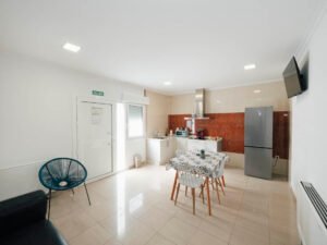 Amplio espacio abierto en el apartamento de Casa Cancela, Palas de Rei, que integra salón con sofá negro y silla de diseño, zona de comedor y cocina totalmente equipada al fondo.