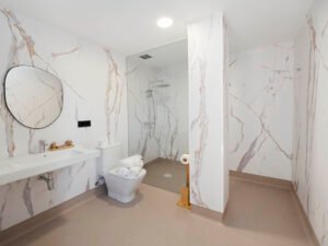 Amplio baño de diseño moderno en Casa Cancela, Palas de Rei, con paredes de mármol, ducha a ras de suelo, espejo de forma orgánica y acabados de lujo para el máximo confort.