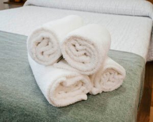 Primer plano de toallas blancas esponjosas presentadas sobre una cama recién hecha en Casa Cancela, resaltando la limpieza y el cuidado en el servicio de este alojamiento rural en Palas de Rei.
