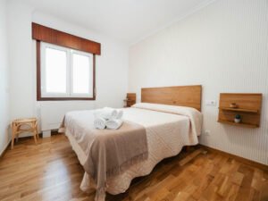 Habitación de matrimonio acogedora en Casa Cancela, Palas de Rei, con cabecero de madera, textiles en tonos tierra y suelo de madera natural.