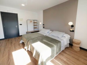 Habitación con dos camas individuales en Casa Cancela, Palas de Rei, con diseño moderno, iluminación cálida y mobiliario funcional para peregrinos del Camino de Santiago.