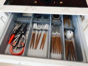 Vista interior de un cajón de cocina en el apartamento de Casa Cancela, mostrando cubertería de diseño con mango de madera y utensilios de cocina organizados y limpios para el uso de los huéspedes en Palas de Rei.