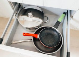 Interior de un cajón de cocina en el apartamento de Casa Cancela con ollas de acero inoxidable y sartenes antiadherentes de diferentes tamaños, todo limpio y organizado para los huéspedes en Palas de Rei.