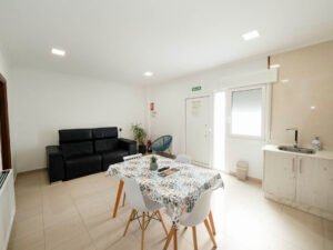 Salón del apartamento de Casa Cancela en Palas de Rei, con un cómodo sofá de cuero negro, zona de comedor luminosa y acceso principal, ideal para el descanso de grupos y familias en el Camino de Santiago.