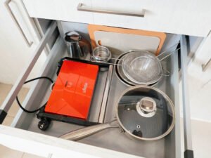 Interior de un cajón del apartamento de Casa Cancela con menaje completo: sandwichera, sartén, cafetera italiana, coladores y tablas de cortar, ideal para estancias largas en el Camino de Santiago.